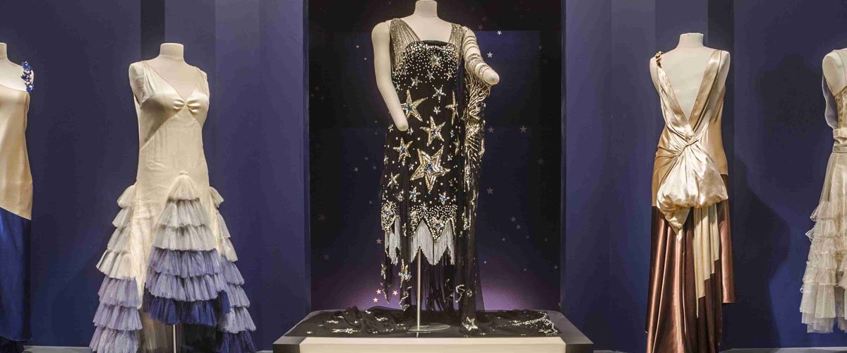 Image of five evening gowns displayed theatrically in Roaring Twenties exhibition