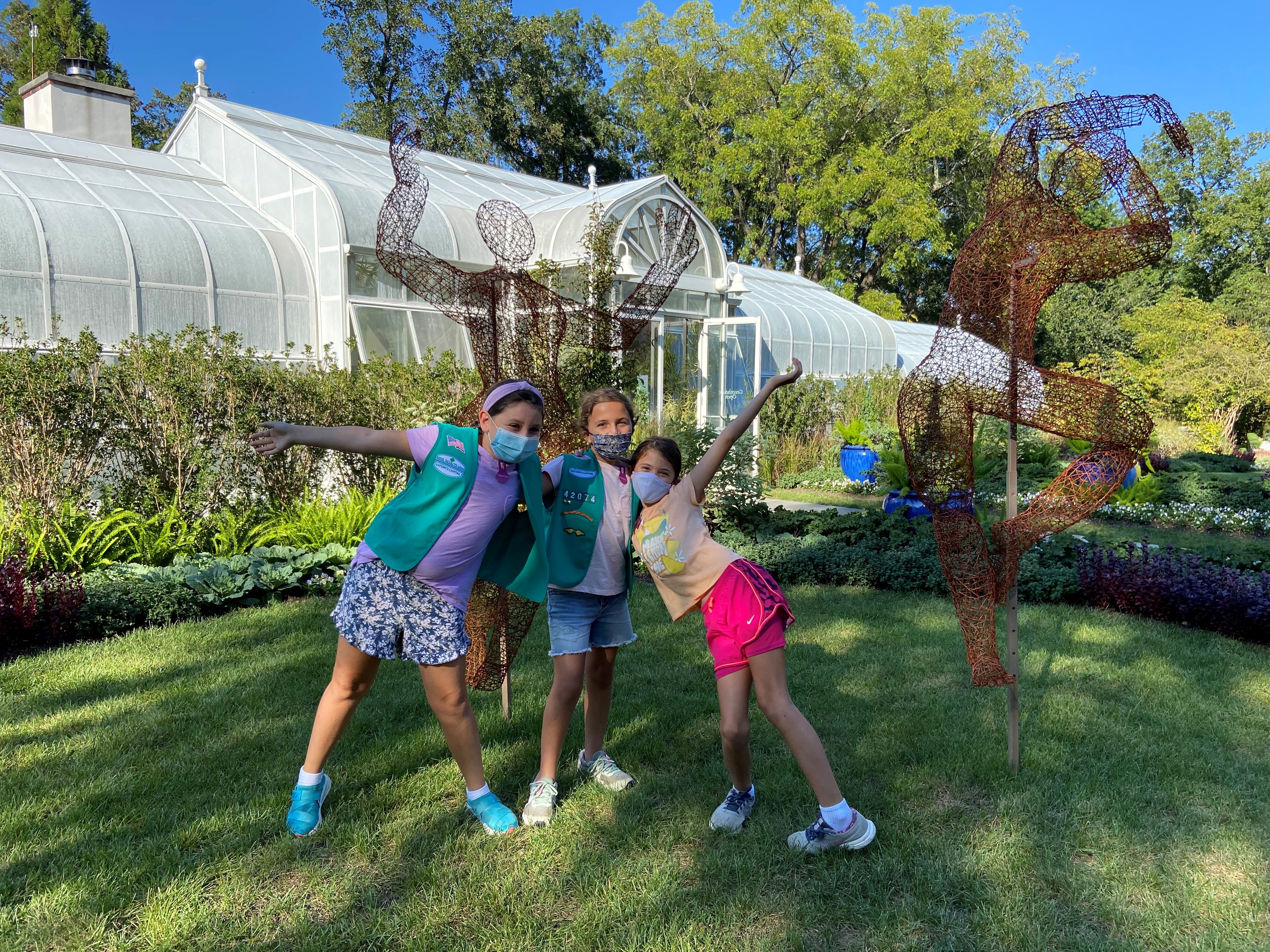 Girl Scouts pose in front of a wire statue by artist Kristine Mays displayed on the lawn in front of Hillwood's greenhouse.