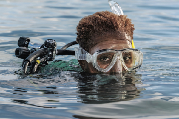 Image of Tara Roberts, a diver, emerging from the water, with just the top half of her face and goggles visible.