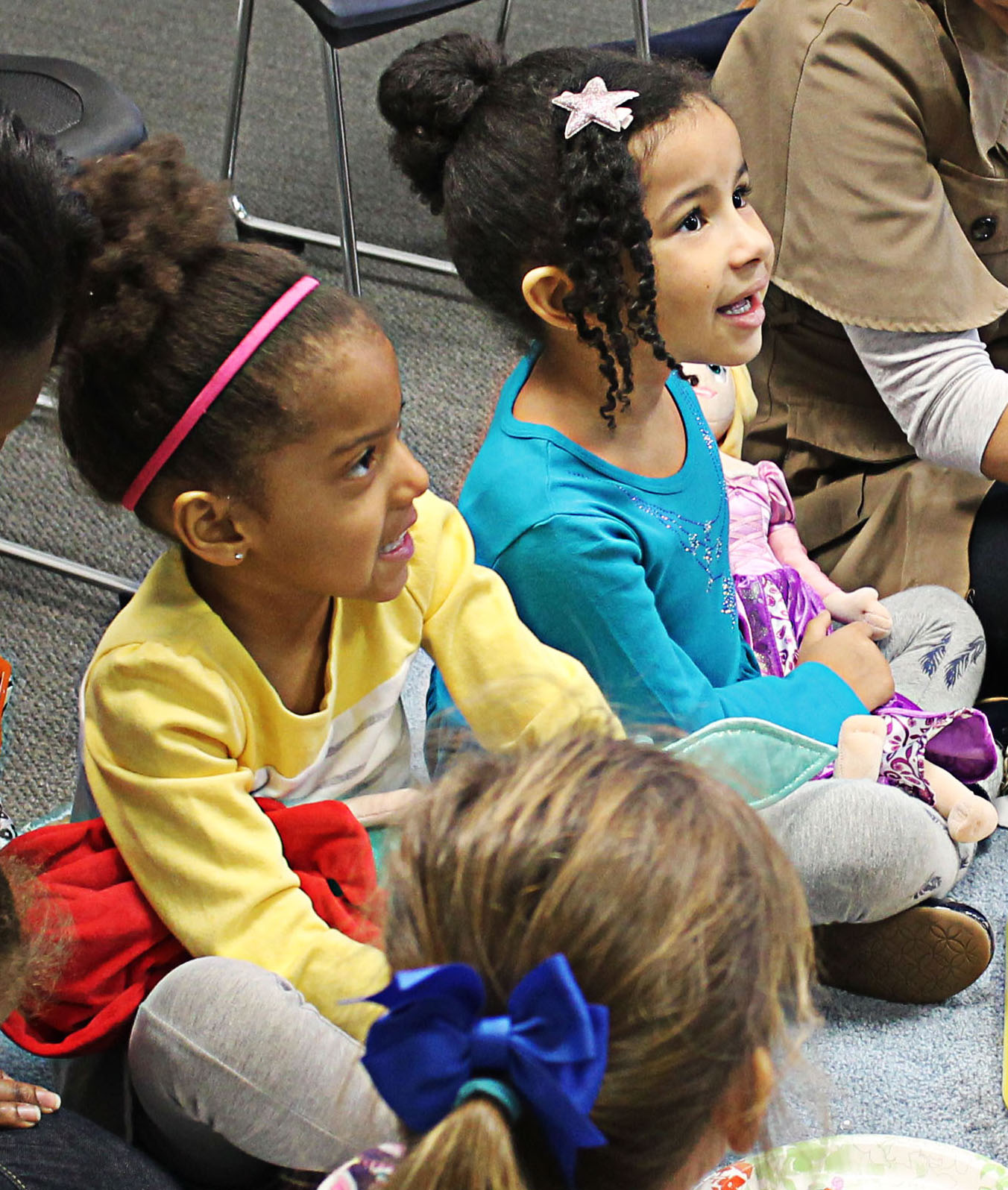 Preschoolers sit on a carpet ready to work on their art project.