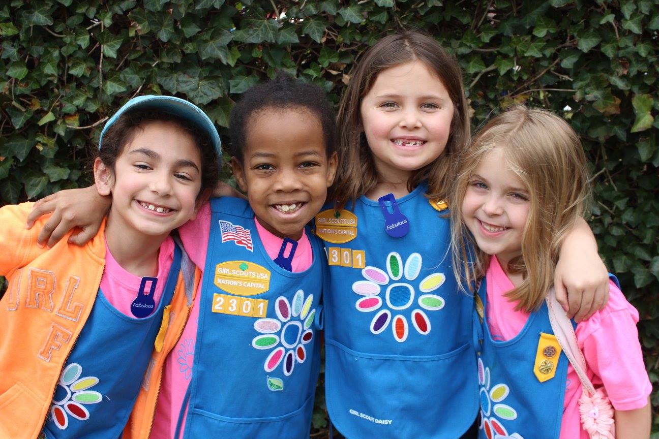 A group of 4 Daisy Girl Scouts wearing their uniforms and smiling at the camera